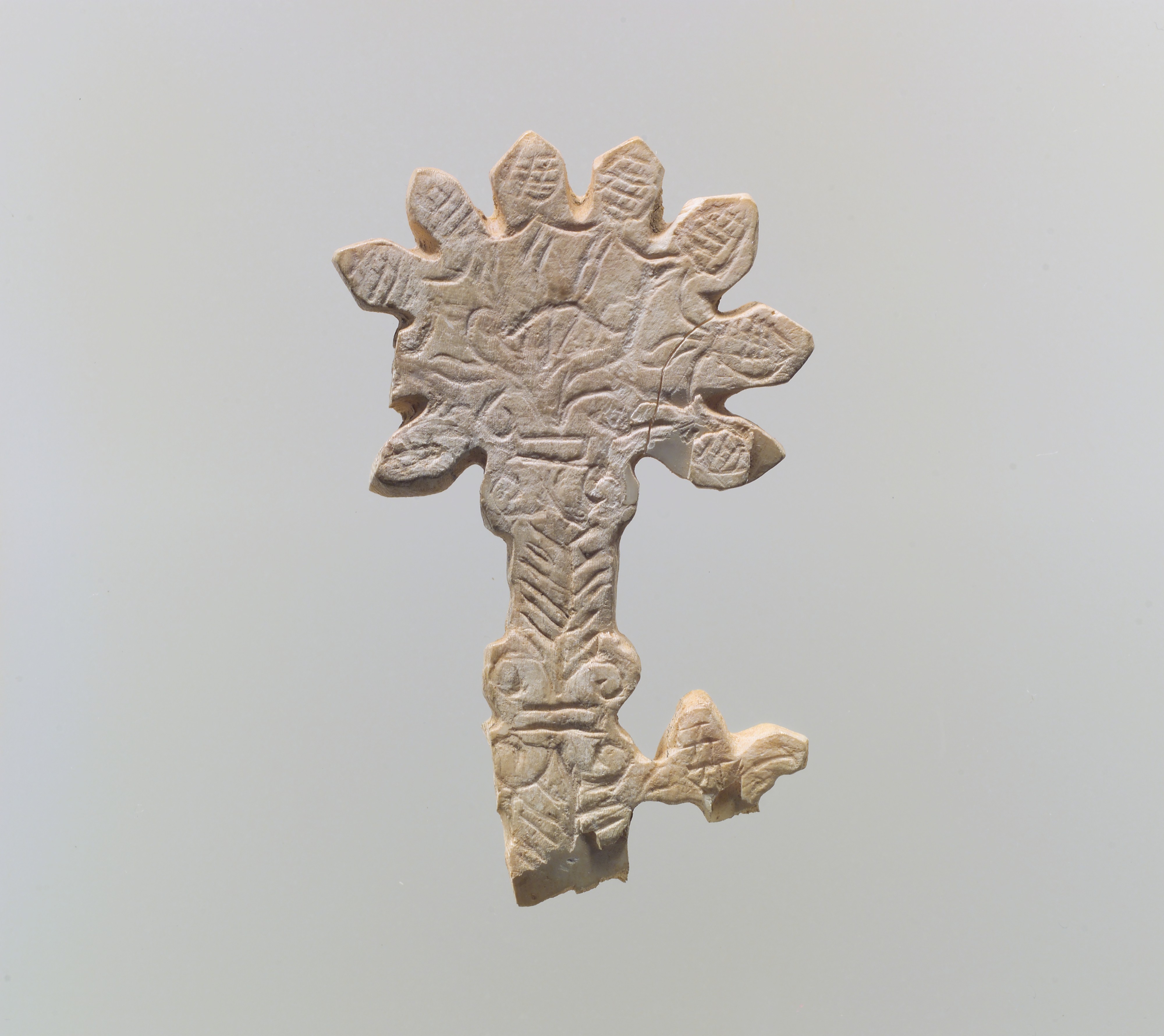 A small Assyrian shell plaque incised with a branching tree, with several broken edges.